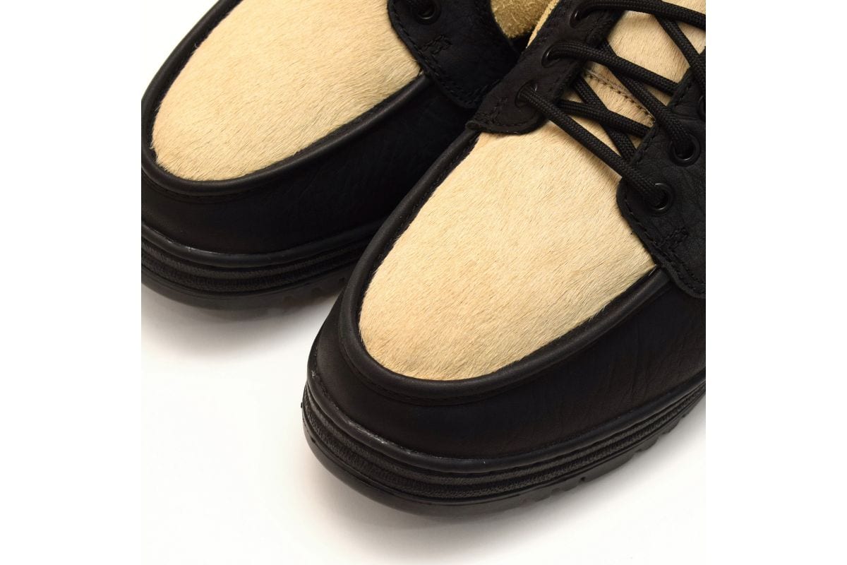 全体をブラックとクリームのコンビネーションカラーに仕上げ、アッパーのメイン素材に独特なシボ感のブラックレザーを採用