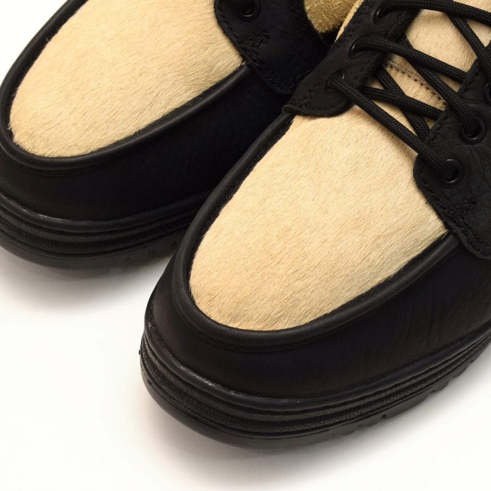 全体をブラックとクリームのコンビネーションカラーに仕上げ、アッパーのメイン素材に独特なシボ感のブラックレザーを採用