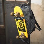 リュック下部に収納されたホルダーとフロント上部のベルトで、スケートボードを取り付けられる