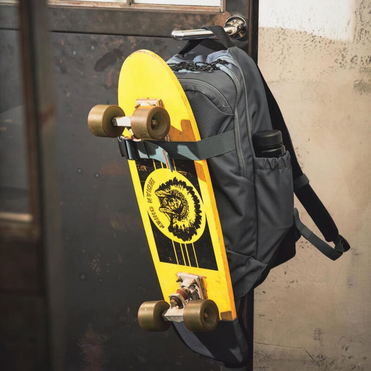 リュック下部に収納されたホルダーとフロント上部のベルトで、スケートボードを取り付けられる